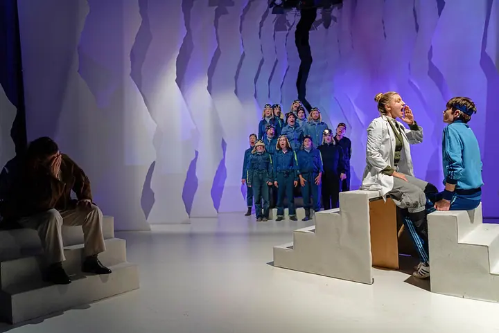 Gebärden der Geschichte mit zwei Darstellerinnen und Ensemble vor blau-violetter Bühnenlandschaft